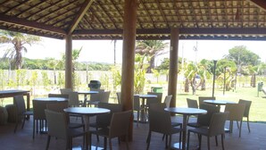 An outdoor patio with round tables and wicker chairs, surrounded by a wooden pergola. - 3/4 Village in Quinta das Lagoas Reserva - Itacimirim Beach  (Camaçari)