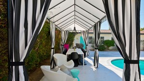 Ein überdachter Außenbereich mit Pool im Hintergrund.