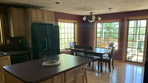 A kitchen with wooden cabinets, a refrigerator, a dining table with chairs, and large windows. - Lake Superior Waterfront home (Brimley)
