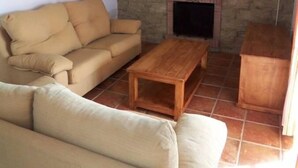 Ett vardagsrum med en vägg av sten, en öppen spis, en beige soffa och ett soffbord i trä.
