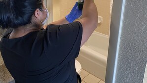 Una persona utilizando un dispositivo portátil verde en un baño con bañera, ducha e inodoro.