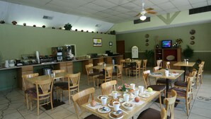 Un restaurante con mesas y sillas de madera, una barra con una máquina de café y un televisor en la pared.