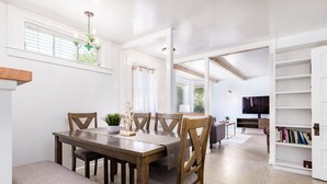 Un comedor con una mesa de madera, sillas, un banco, una araña y una estantería.