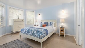 Un dormitorio con cama, mesitas de noche, cómoda y ventana con persianas.