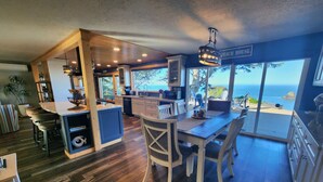 A spacious kitchen with wooden flooring, a dining area with a view of the ocean, and a sign indicating 'BEACH HOUSE'. - Ocean Front Home- spacious, beautiful yard, hot tub & ocean view all around!! (Brookings)
