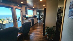 Um corredor com piso de madeira, uma área de estar com cadeiras, uma cozinha e vista para o oceano.