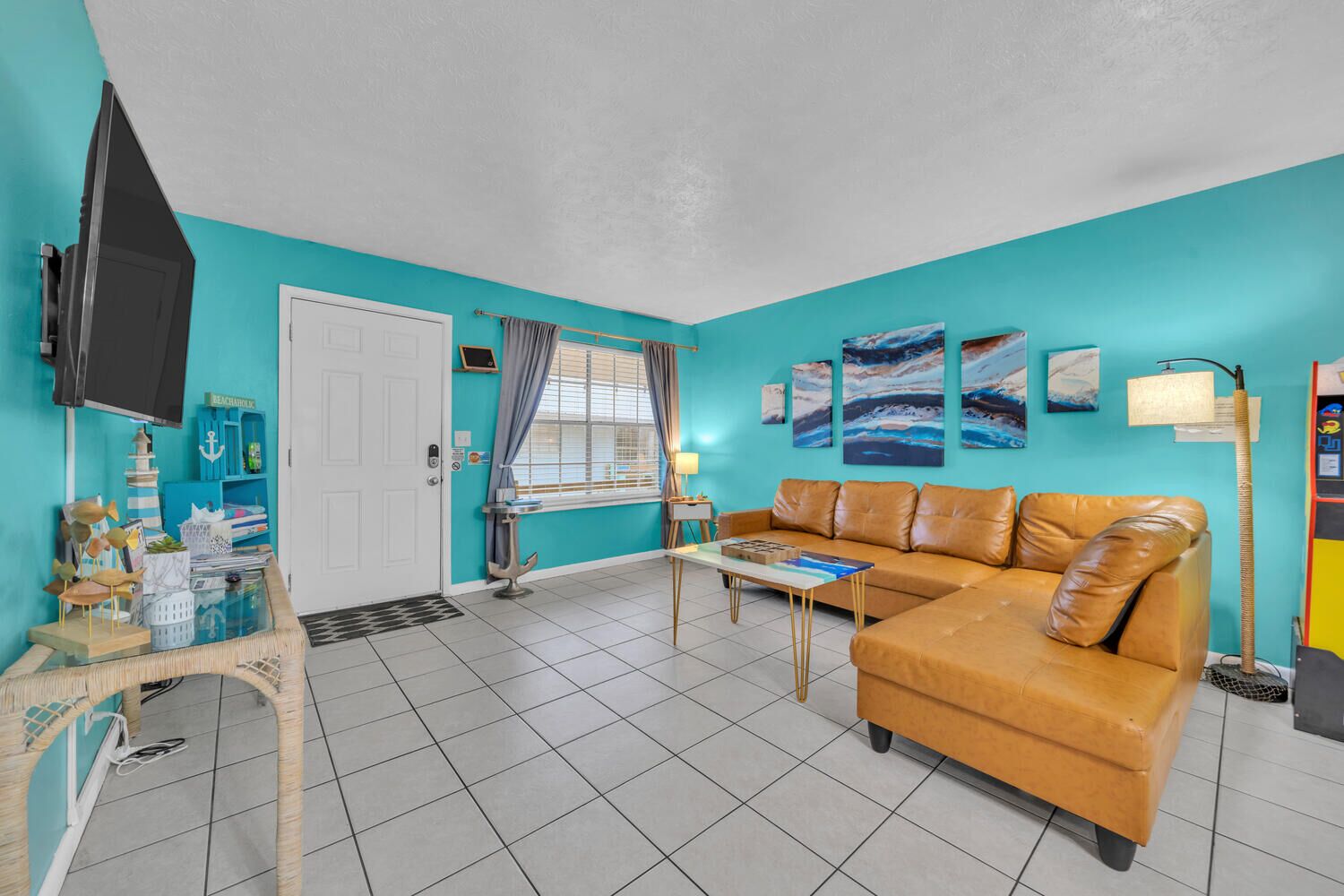 A living room with a teal wall, a brown leather sofa, a television, and a coffee table.