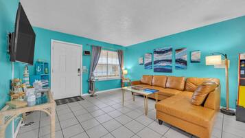 A living room with a teal wall, a brown leather sofa, a television, and a coffee table.
