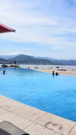 An infinity pool with a view of a beach and mountains.