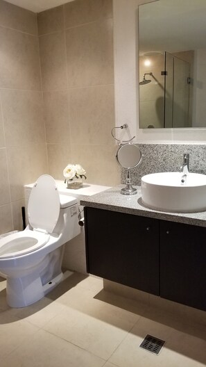 A bathroom with a toilet, sink, mirror, and a shower area.
