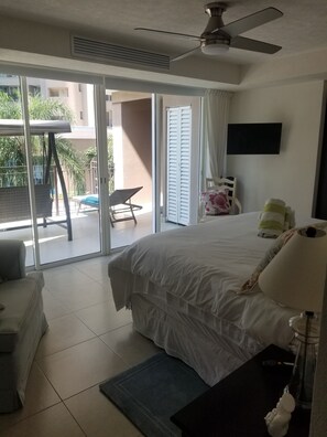 A hotel room with a bed, a desk, a chair, a TV, and a balcony with a chair and a table.