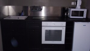 A compact kitchen with dark cabinets, a white sink, a microwave, a small oven, and a refrigerator.