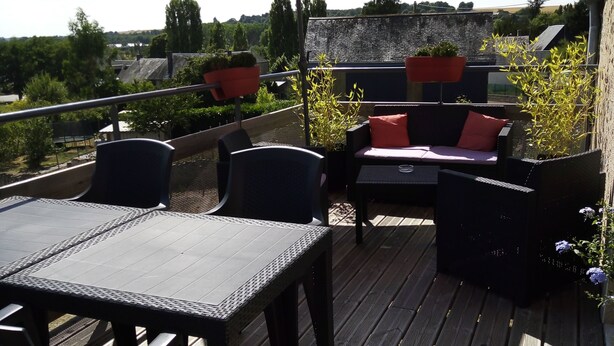 An outdoor patio with a table and chairs, a red umbrella, and potted plants.