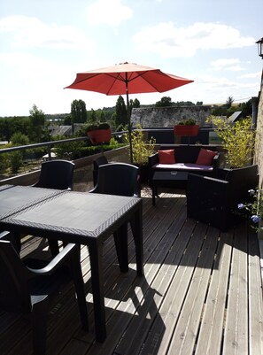 An outdoor patio with a table and chairs, a red umbrella, and potted plants.
