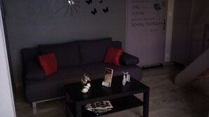 A modern living room with a dark grey sofa, red cushions, a coffee table with magazines, a white chair, and a wall with butterfly decals.