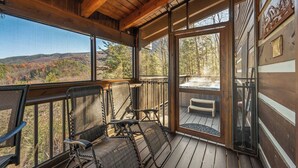 Eine Holzdielen-Terrasse mit zwei Schaukelstühlen und einer Bank, mit Blick auf eine malerische Herbstlandschaft und Hügel.