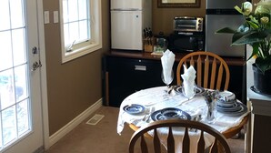 A compact kitchen with a dining table set for two, a refrigerator, a toaster, and a potted plant. - Willow Pond Bed and Breakfast  (Port Perry)