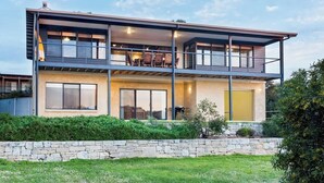 A modern two-story house with a balcony, large windows, and a stone wall in front. - Breakaway: Bay Views, Games & Beach Bliss (Gracetown)