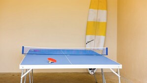 A ping pong table with a paddle and a surfboard leaning against the wall. - Breakaway: Bay Views, Games & Beach Bliss (Gracetown)