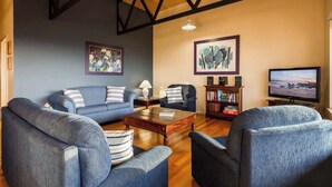 A living room with a blue sofa, two armchairs, a coffee table, and a TV. - Breakaway: Bay Views, Games & Beach Bliss (Gracetown)