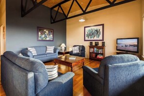 Una sala de estar con un sofá azul, dos sillones, una mesa de centro y un televisor.