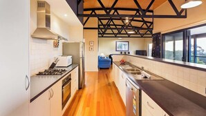 A modern kitchen with a wooden ceiling, stainless steel appliances, and a view through large windows. - Breakaway: Bay Views, Games & Beach Bliss (Gracetown)