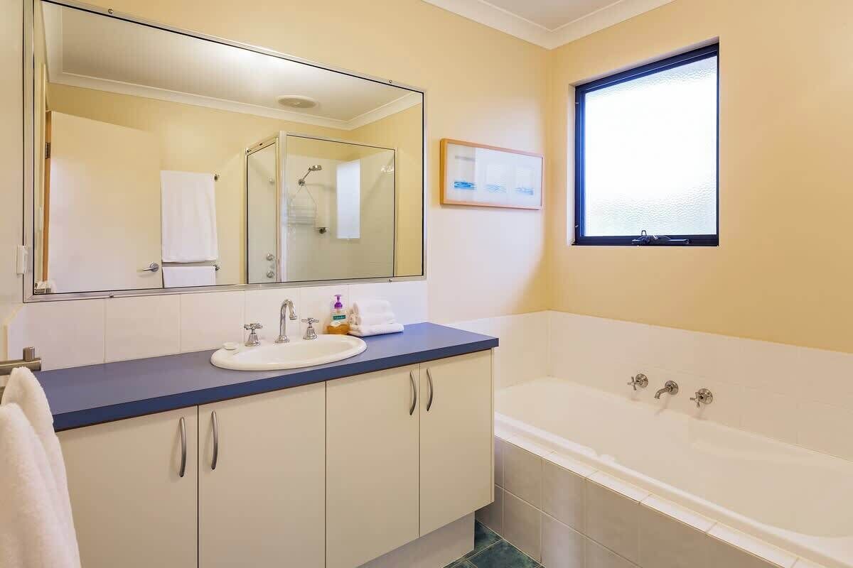 A bathroom with a bathtub, a sink, a mirror, and a window.