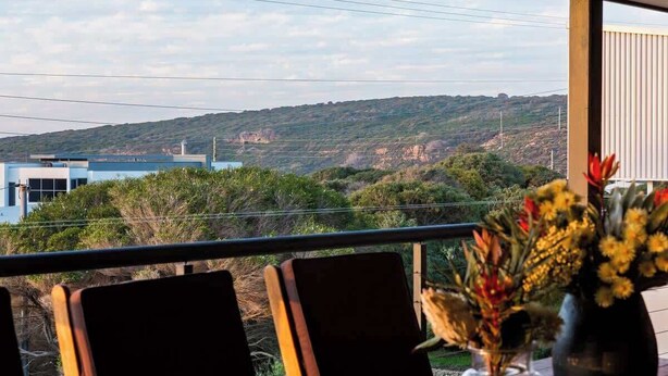 A dining area with a view of a hilly landscape, a table with chairs, and a vase with flowers. - Breakaway: Bay Views, Games & Beach Bliss (Gracetown)