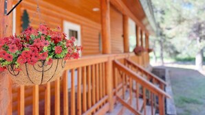 A wooden cabin with a porch and a hanging flower basket. - Hot Tub  | Fire Pit | 32 Miles to YNP | Fox Den Cabin (Island Park)