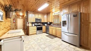 A kitchen with wooden cabinets, stainless steel appliances, and a tiled floor. - Hot Tub  | Fire Pit | 32 Miles to YNP | Fox Den Cabin (Island Park)