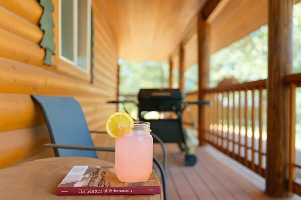 A wooden deck with a table holding a drink and a book.