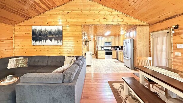 A cabin interior with a wooden ceiling, a sofa, a dining table, and a kitchen area. - Hot Tub  | Fire Pit | 32 Miles to YNP | Fox Den Cabin (Island Park)
