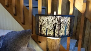 A wooden nightstand with a lamp featuring a tree design, a gray sofa with a quilted pillow, and a wooden staircase in the background.