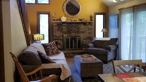 A cozy living room with a fireplace, a sofa, a rocking chair, and a dining table.