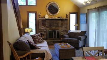A cozy living room with a fireplace, a sofa, a rocking chair, and a dining table.