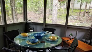 A round glass table with blue and yellow bowls, black wicker chairs, and a view of the outdoors through large windows.