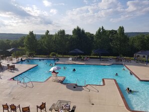 Une piscine dotée de plusieurs couloirs, entourée de chaises longues et de parasols, et offrant une vue sur les arbres et les collines en arrière-plan.