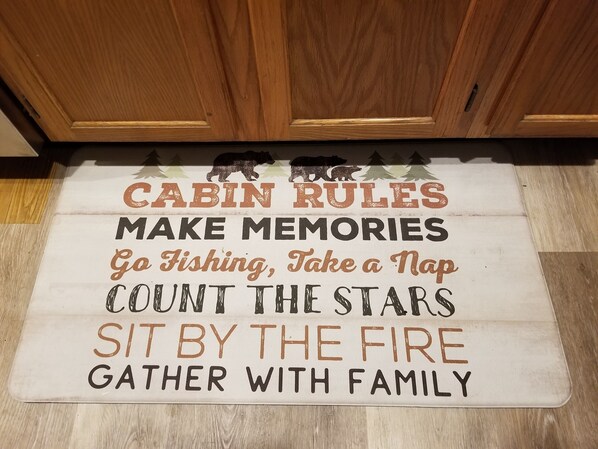 Un tapis orné des règles de la cabane, pour créer des souvenirs inoubliables, avec des activités comme la pêche, l’observation des étoiles et des moments de partage en famille.