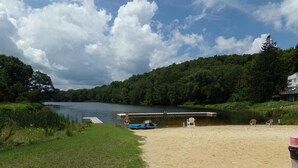 A lakeside beach with a dock, chairs, and a boat.