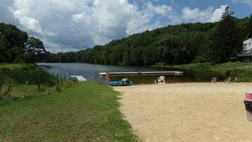 A lakeside beach with a dock, chairs, and a boat.