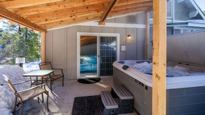 A covered outdoor area with a hot tub, wooden ceiling, and a table with chairs.