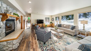 A cozy living room with a stone fireplace, a television, and a large window overlooking a snowy landscape.