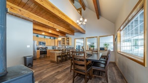 A spacious kitchen with wooden beams, a dining area with a large table and chairs, and a view through a window.