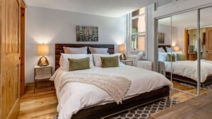 Un dormitorio moderno con una cama grande, cabecera de madera, lámparas de noche, un espejo y suelo de madera.