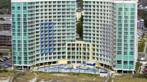 A large hotel with a curved facade, multiple floors, and a central courtyard with outdoor seating. - Luxury oceanfront condo w/ Breathtaking views. Lazy River, pools, hot tubs. (North Myrtle Beach)