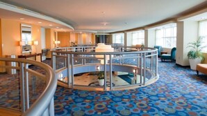 A hotel lobby with a central circular seating area, a lower level with a glass railing, and a patterned carpet. - Luxury oceanfront condo w/ Breathtaking views. Lazy River, pools, hot tubs. (North Myrtle Beach)