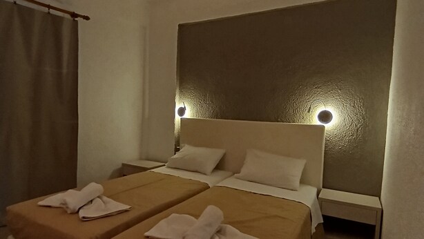 Habitación de hotel con dos camas, una mesita de noche y una lámpara fijada a la pared.