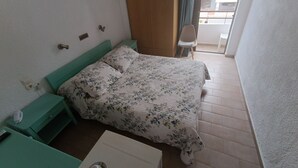 Un dormitorio con cama, mesita de noche, silla y ventana.