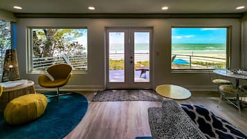 Un salon moderne avec vue sur la plage, comprenant un canapé, des fauteuils, une table à manger et une grande fenêtre.