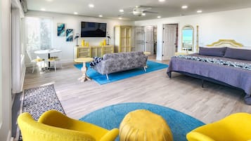 Une chambre moderne avec un lit, un canapé, des chaises jaunes et un téléviseur.